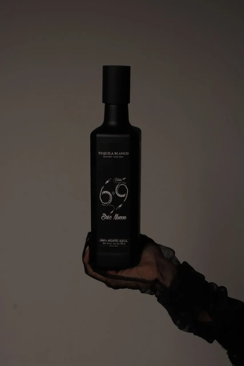 Botella Seis Nueve en la mano sobre fondo gris